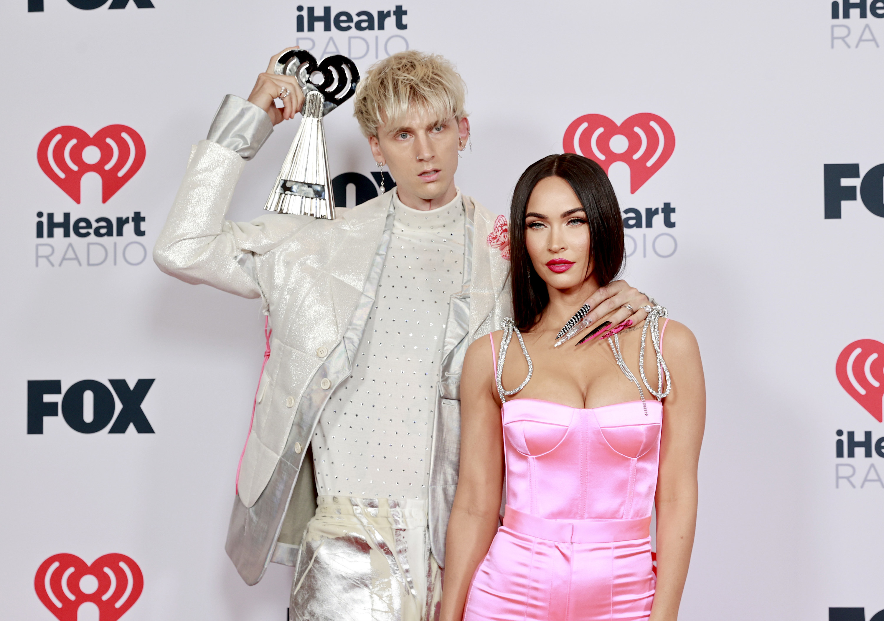 MGK with one arm around Megan&#x27;s neck and the other placing a clutch on his shoulder for a red carpet photo