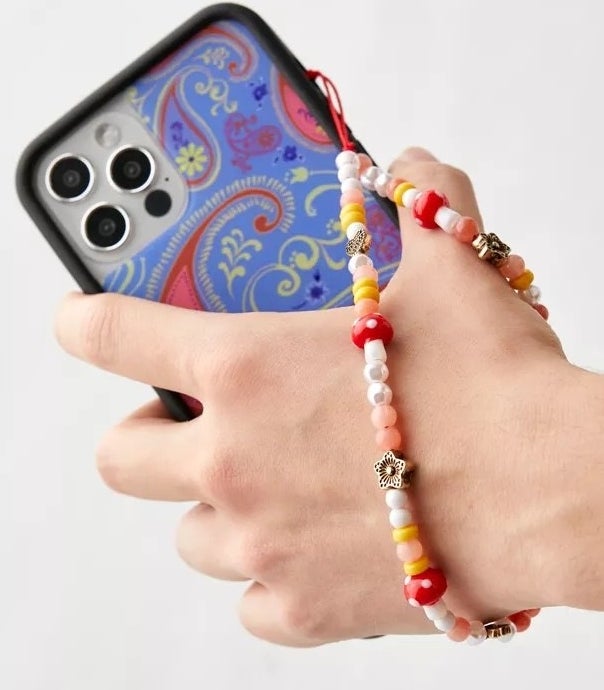 A person holding a cell phone with the wrist strap around their wrist