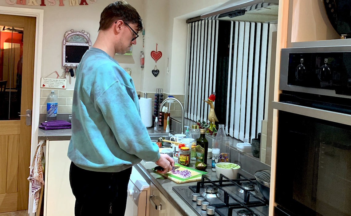 Tall guy stands in kitchen cutting onions