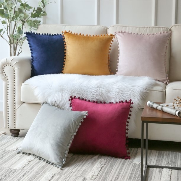 Velvet throw pillows on couch, from left to right navy pillow, yellow pillow, light pink pillow, gray pillow on floor bottom left next to red pillow on floor