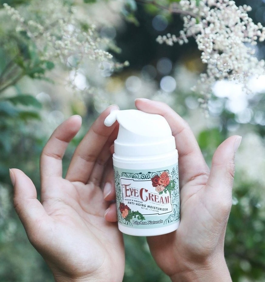 A person holding the eye cream in front of plants