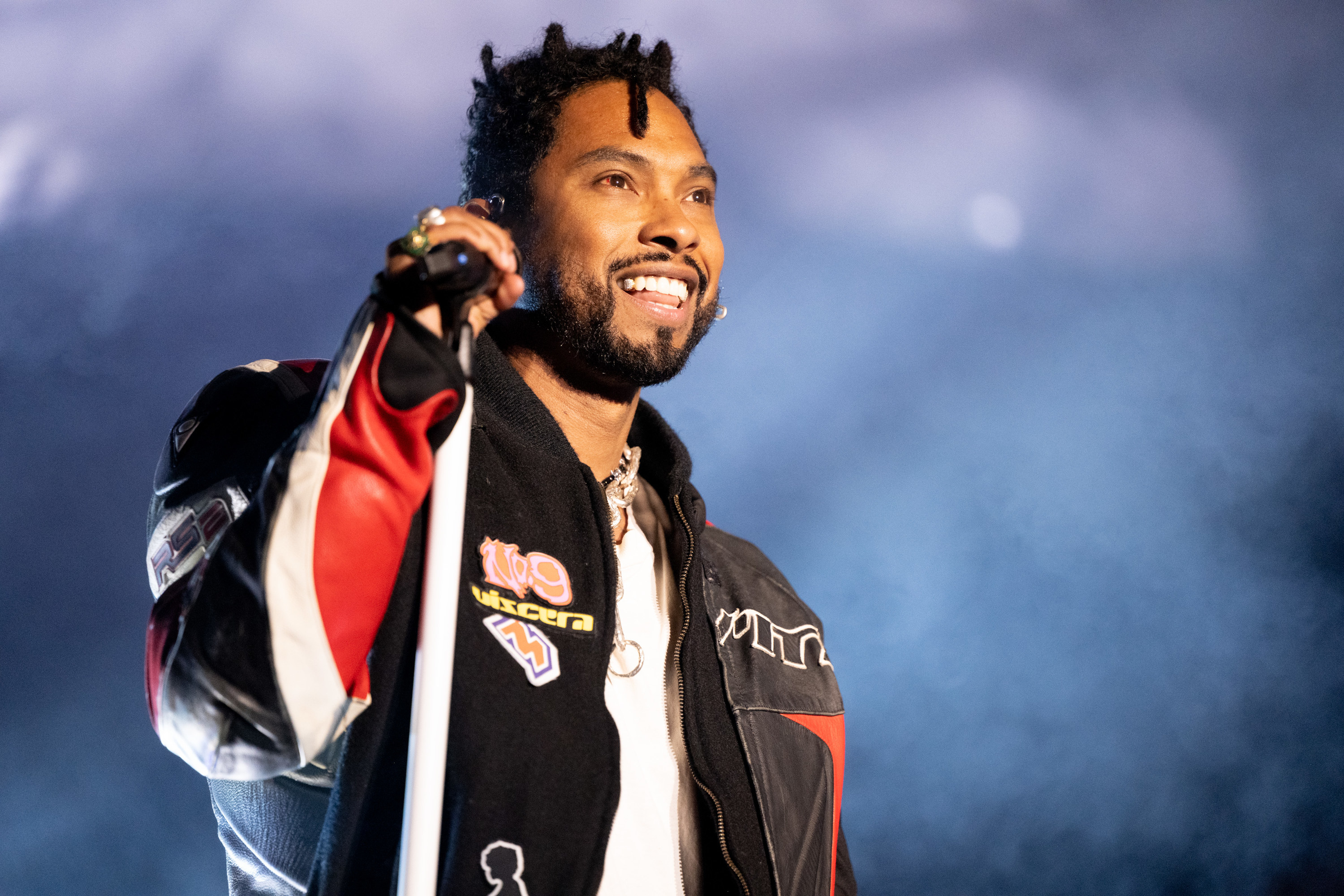 Miguel sings on stage while smiling holding a mic stand in his hand.
