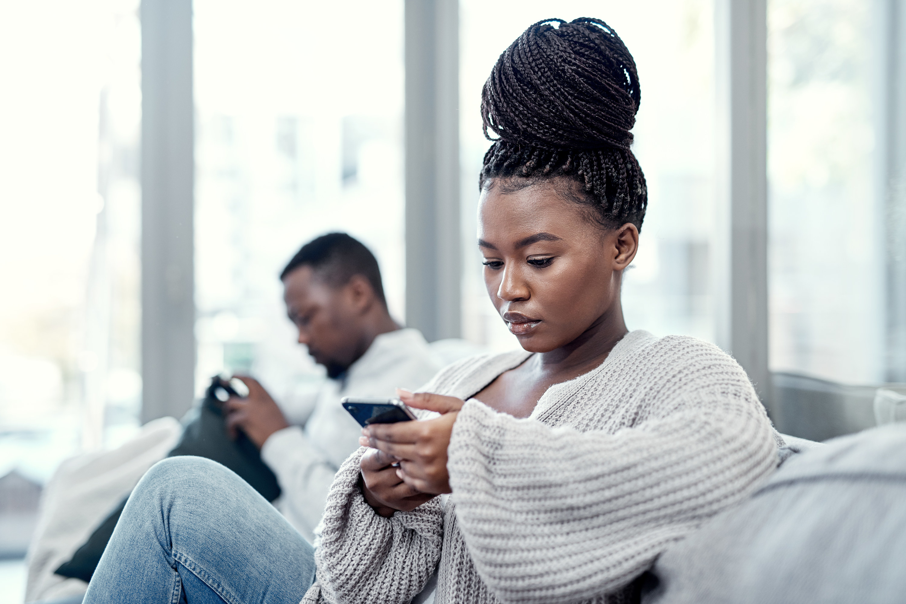 two people sitting apart on the couch on their phone