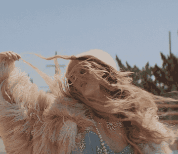 a gif of a person wearing a furry coat and pearls flipping their hair over their shoulder