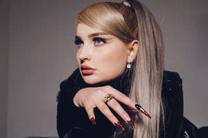 Kim Petras on top of a piano playing it casually with very long nails