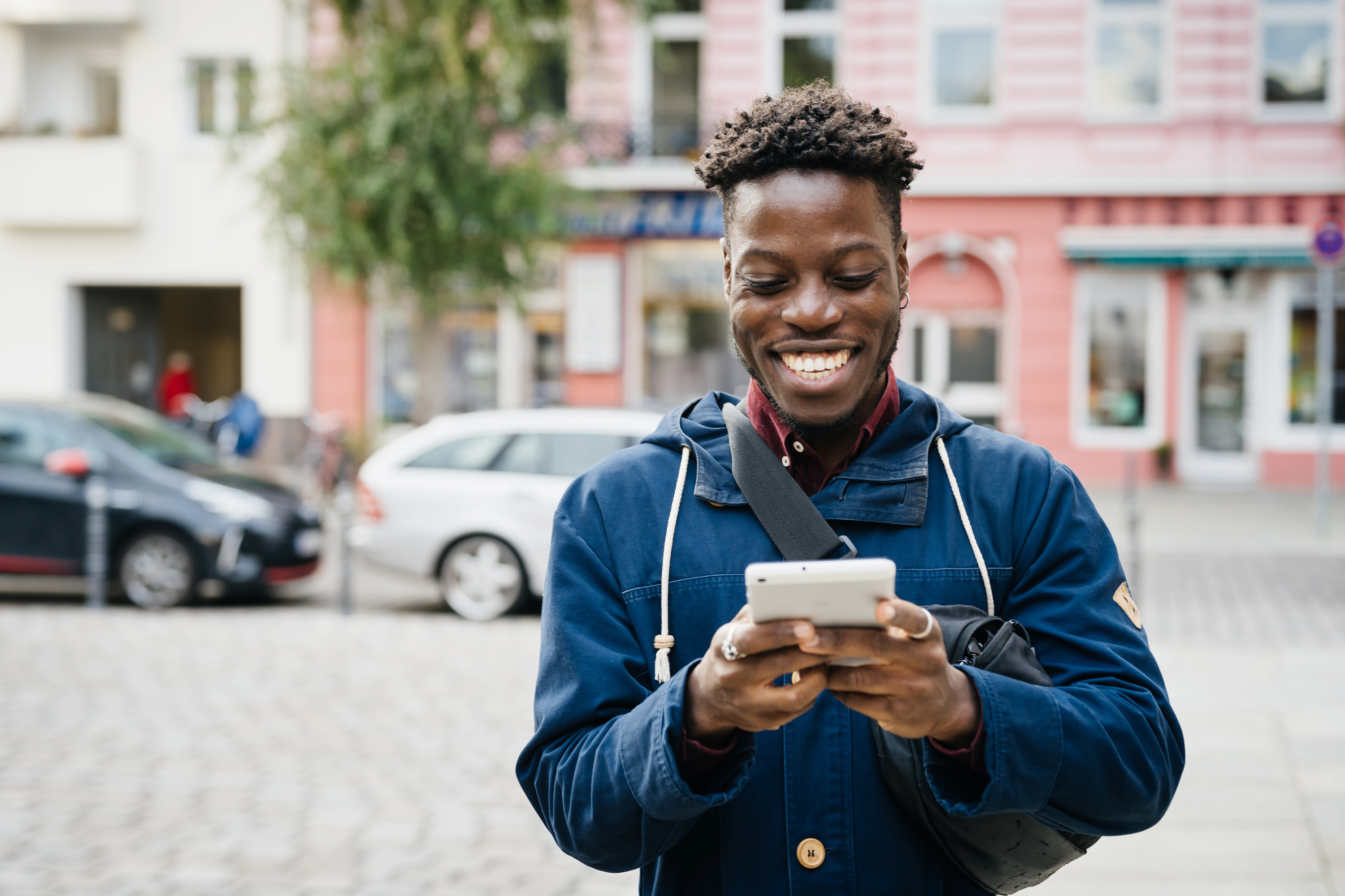 a man smiling at his phone while standing outside