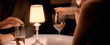two hands touching the rim of glasses at a dinner table