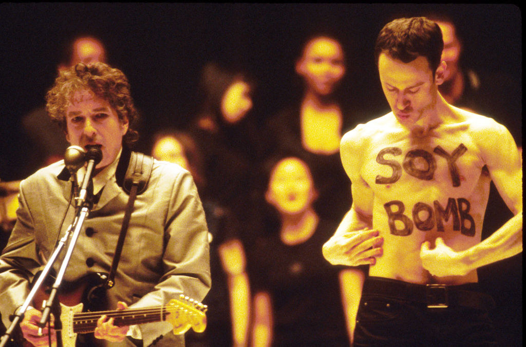 bob dylan being interrupted by a man with soy bomb written on his chest