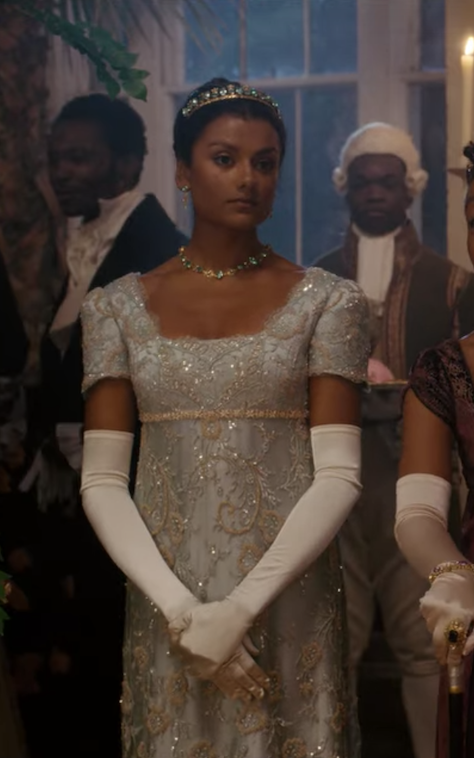 she wears a short-sleeved dress with lots of shiny detailing paired with long gloves and a tiara