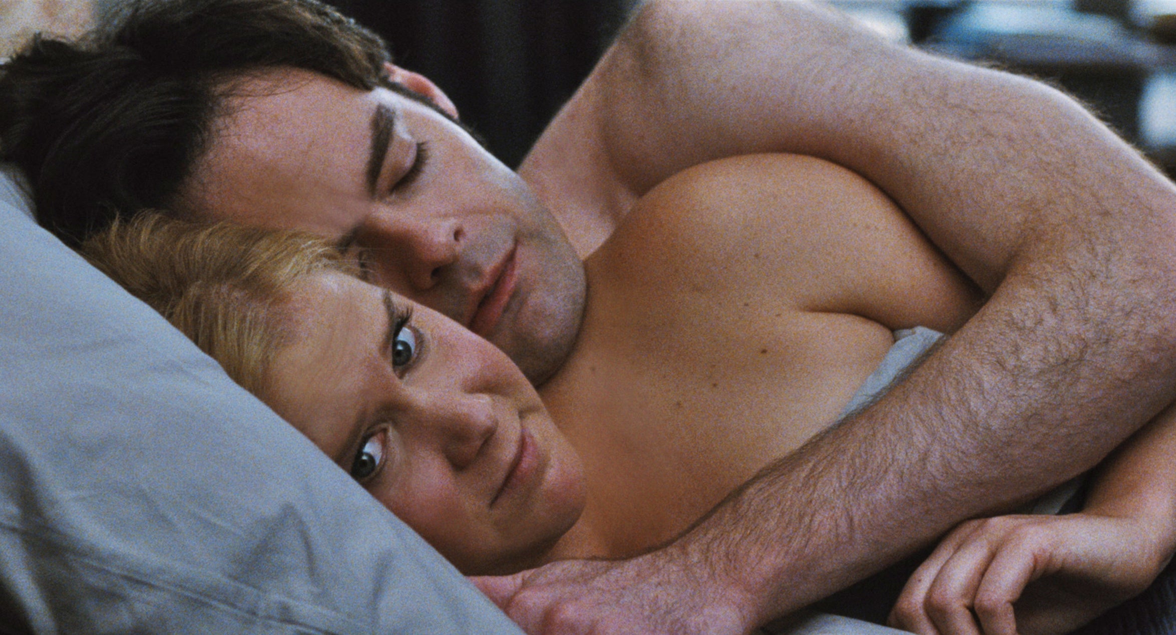 Amy Schumer and Bill Hader cuddling in bed with her looking skeptical