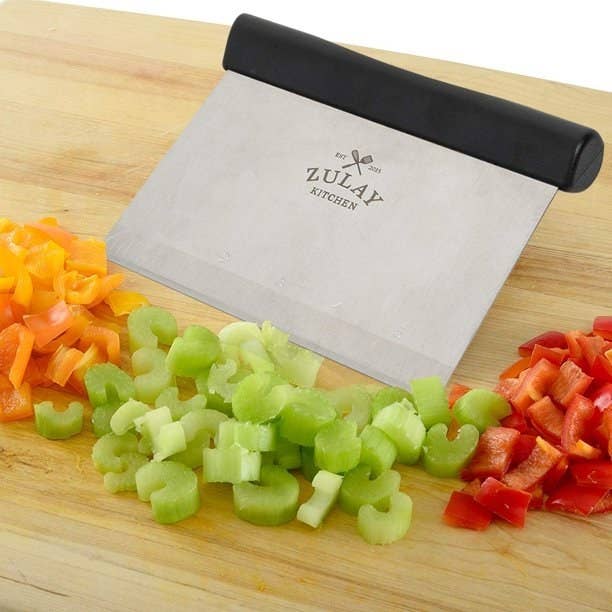 the bench scraper on a cutting board with chopped bell peppers and celery
