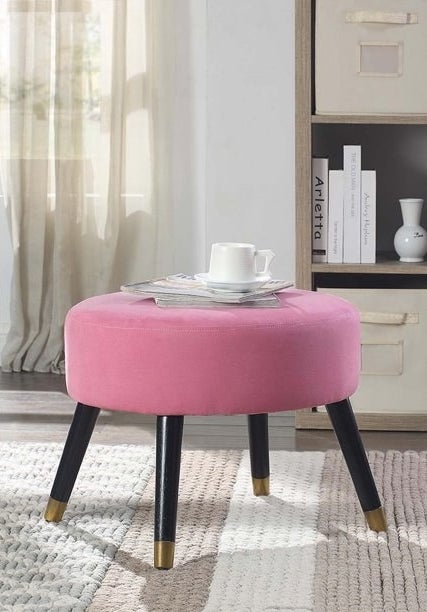 Pink ottoman with black legs, magazines and white coffee cup on top