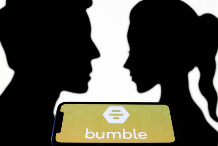 A silhouette of two people facing each other with a phone showing the bumble app in between them