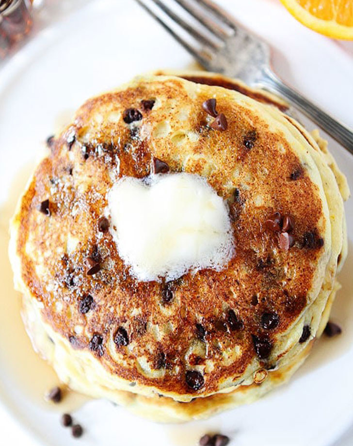 A stack of orange chocolate chip pancakes with butter on top