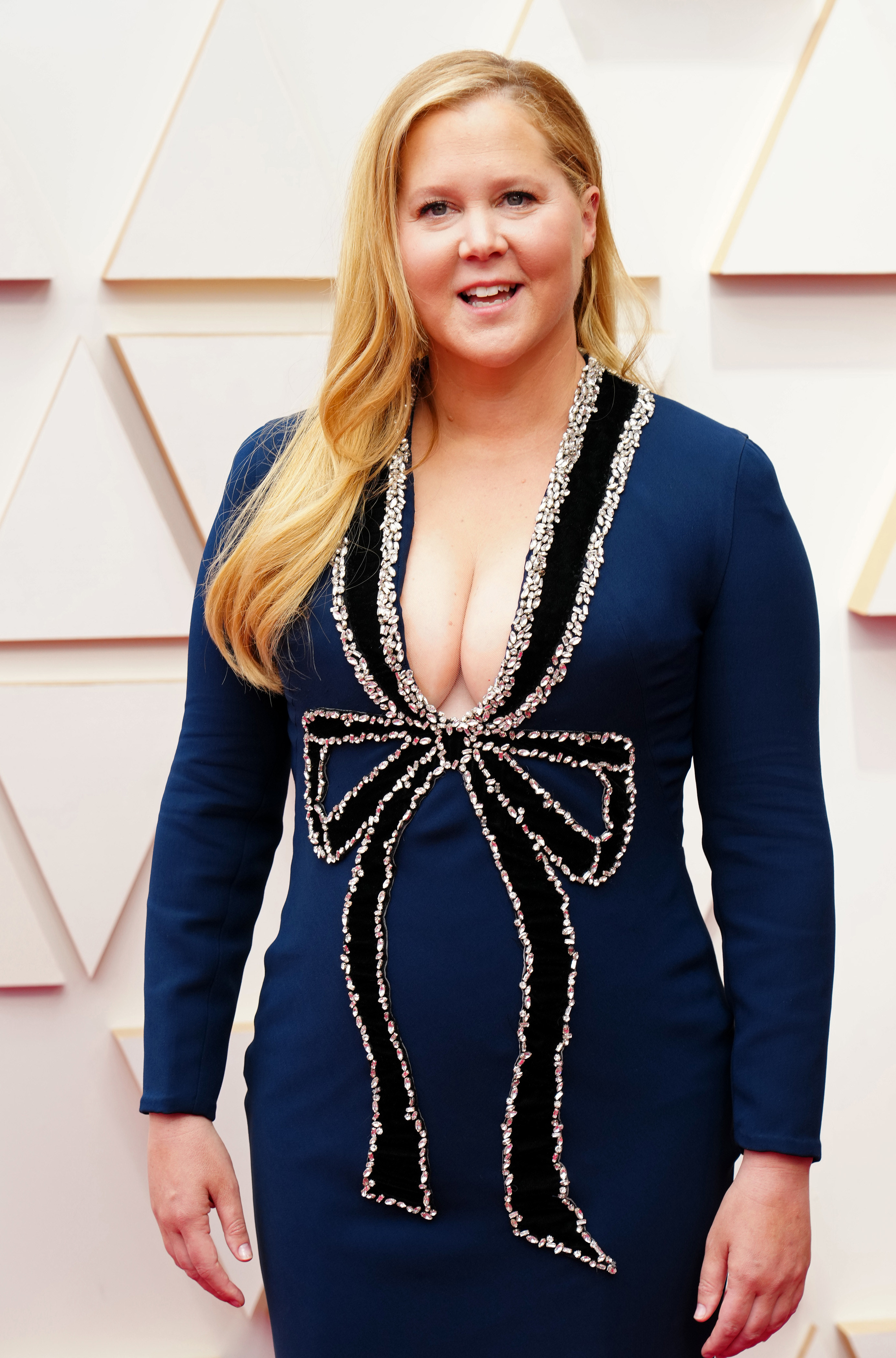 Amy posing on the Oscars red carpet in a long-sleeved form-fitting dress with plunging neckline