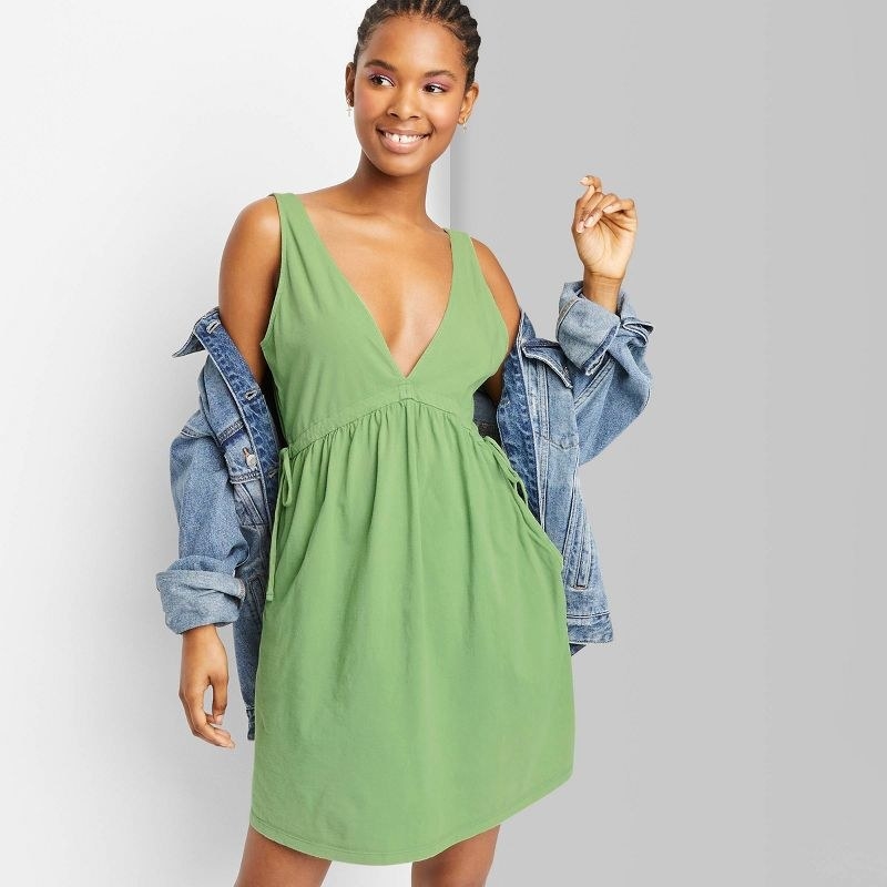 Model wearing the green mini dress with jean jacket shrugged on shoulders
