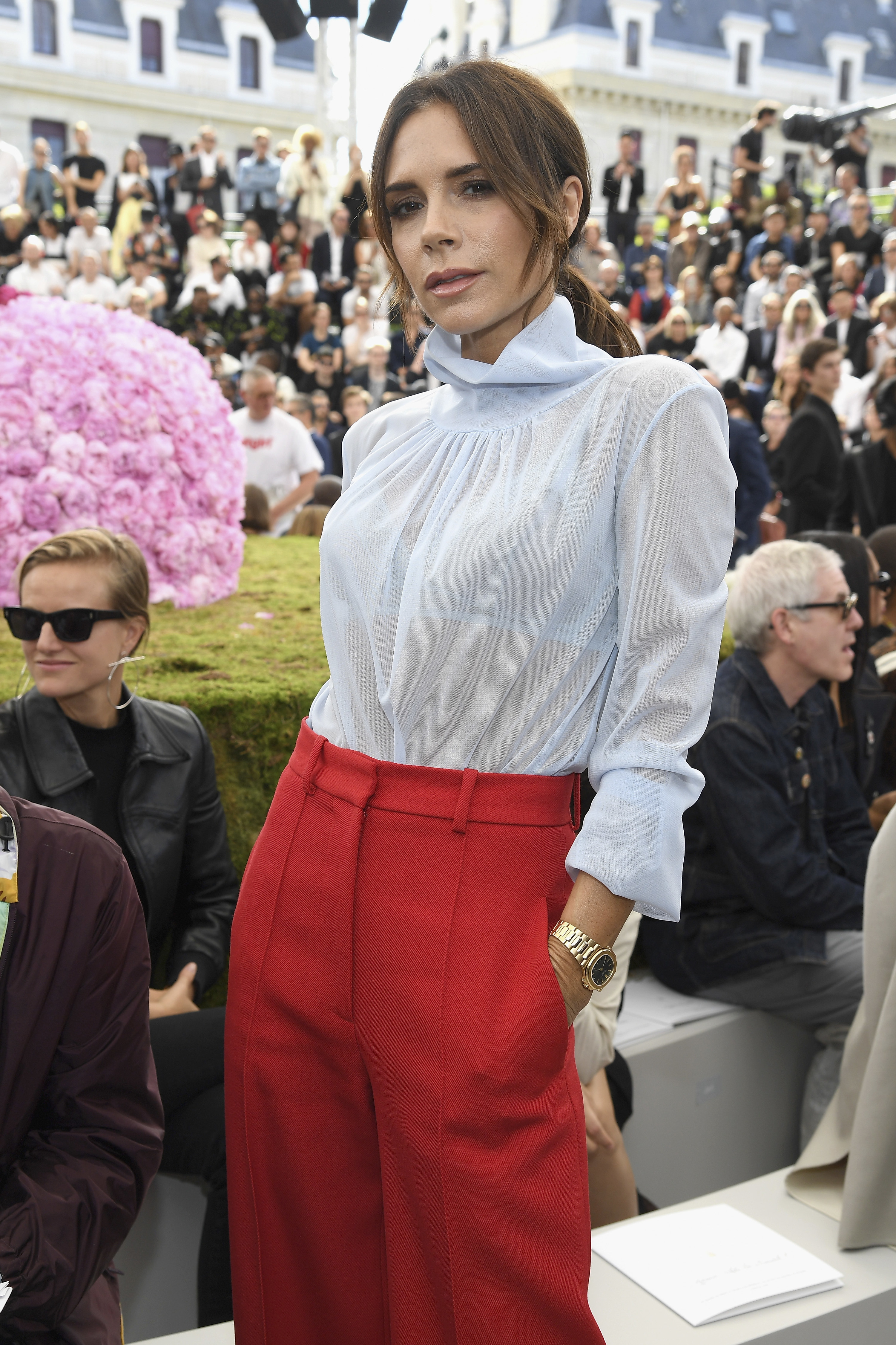 Victoria Beckham stands proudly at a fashion event wearing trousers and a see-through blouse
