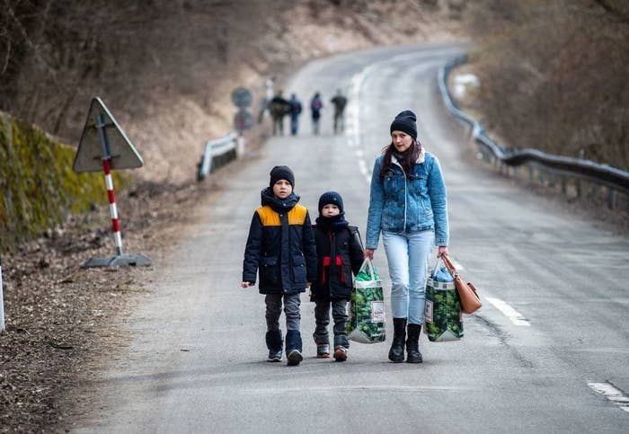 Two small boys and a woman walking with on a road with bags