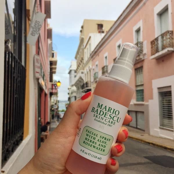 Someone holding a bottle of Mario Badescu facial spray against a cityscape