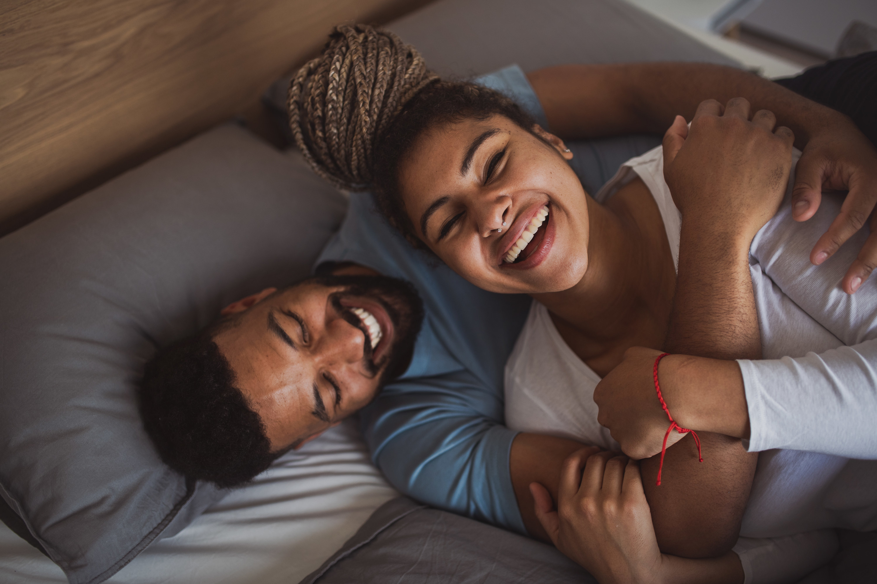 A man and woman laying in bed laughing and hugging each other