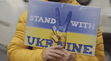 A person holding a sign that says, &quot;Stand with Ukraine&quot;