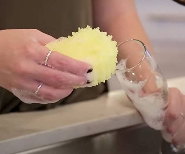 A person using the Scrub Daddy sponge to wash a champagne flute