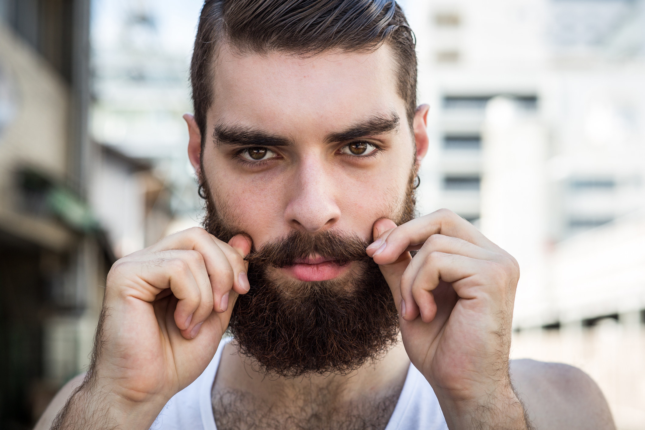 A bearded hipster twists the ends of his mustache while looking into the camera