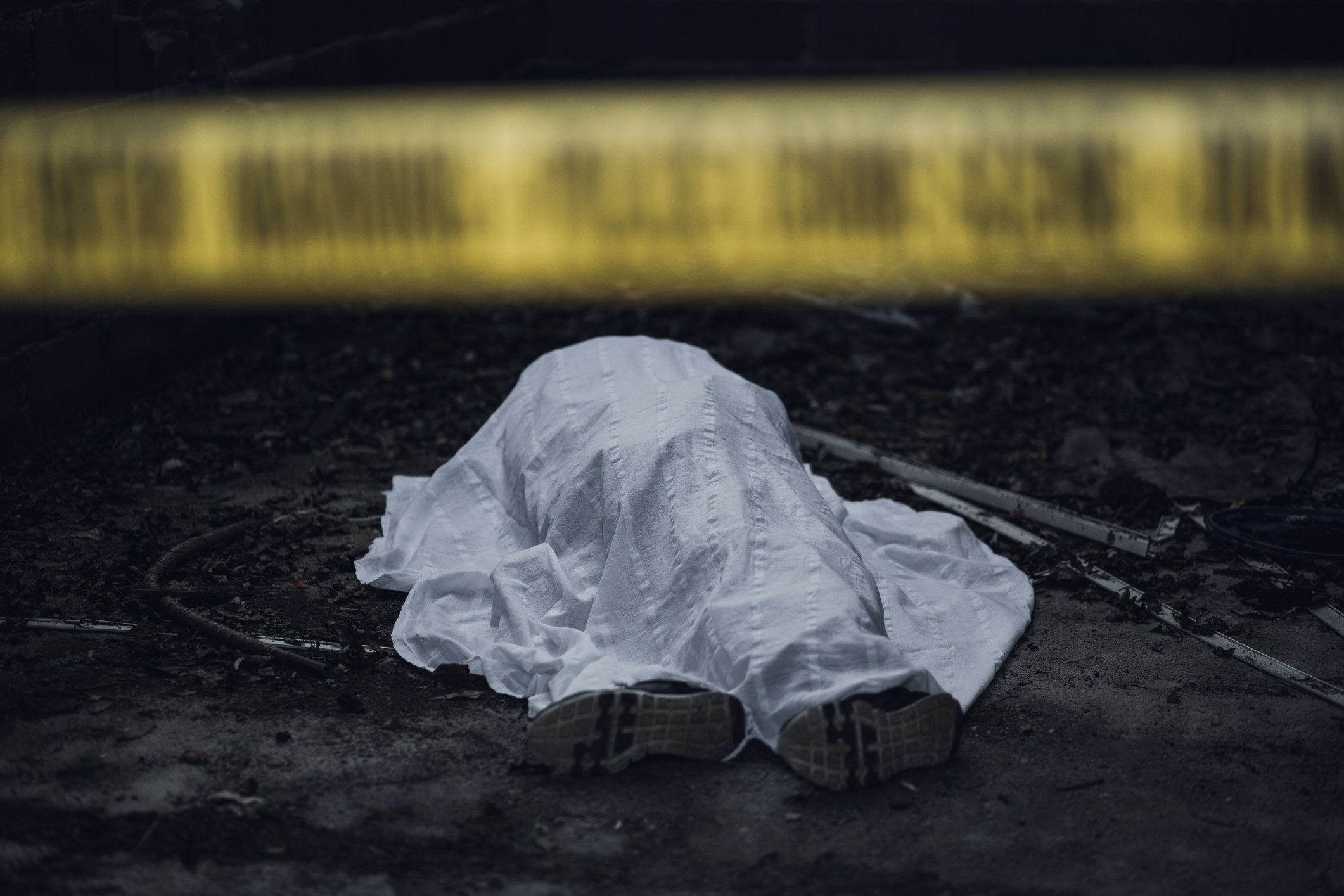 A covered dead body behind crime scene tape