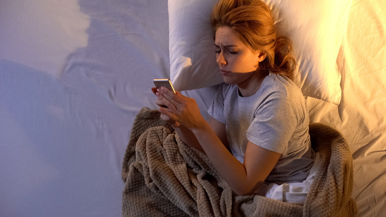 Woman lying in bed and looking at her cellphone