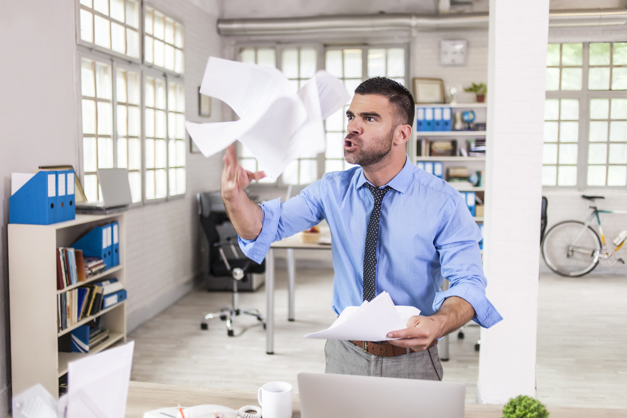 Man in a tie throwing papers in the air in frustration