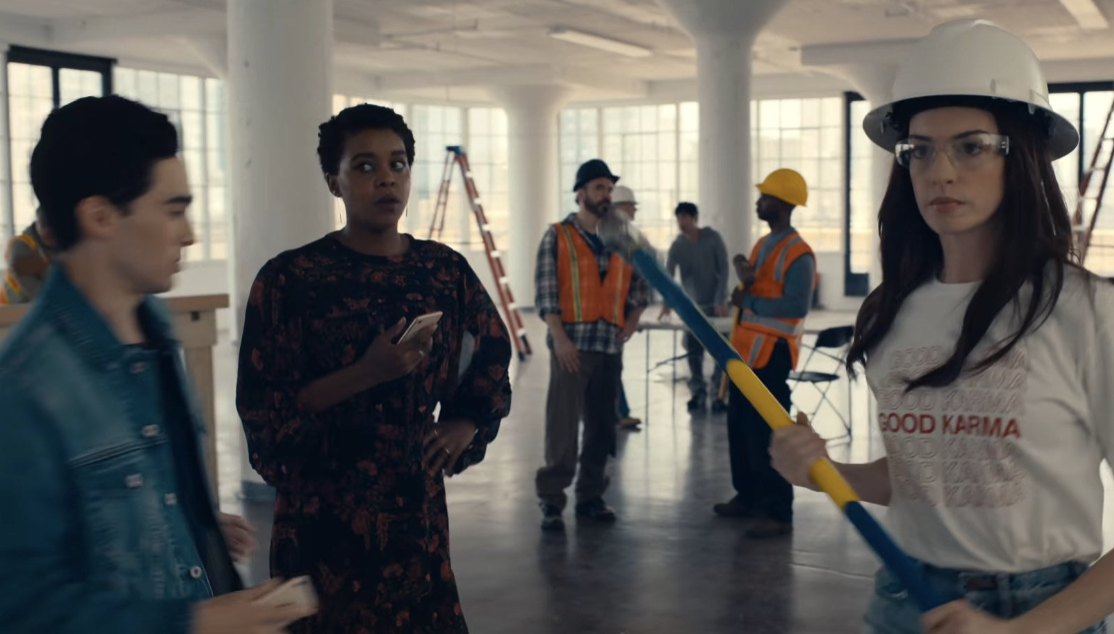 Anne Hathaway carries a hammer while her staff looks on