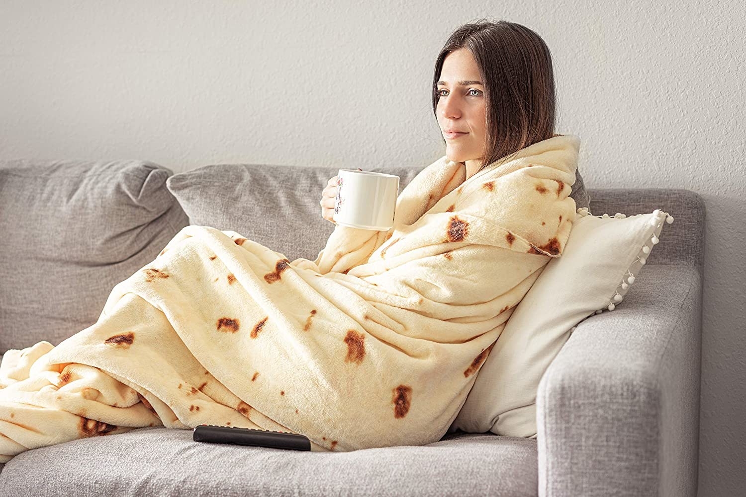 a person snuggling on a sofa while swaddled in a burrito-esque blanket