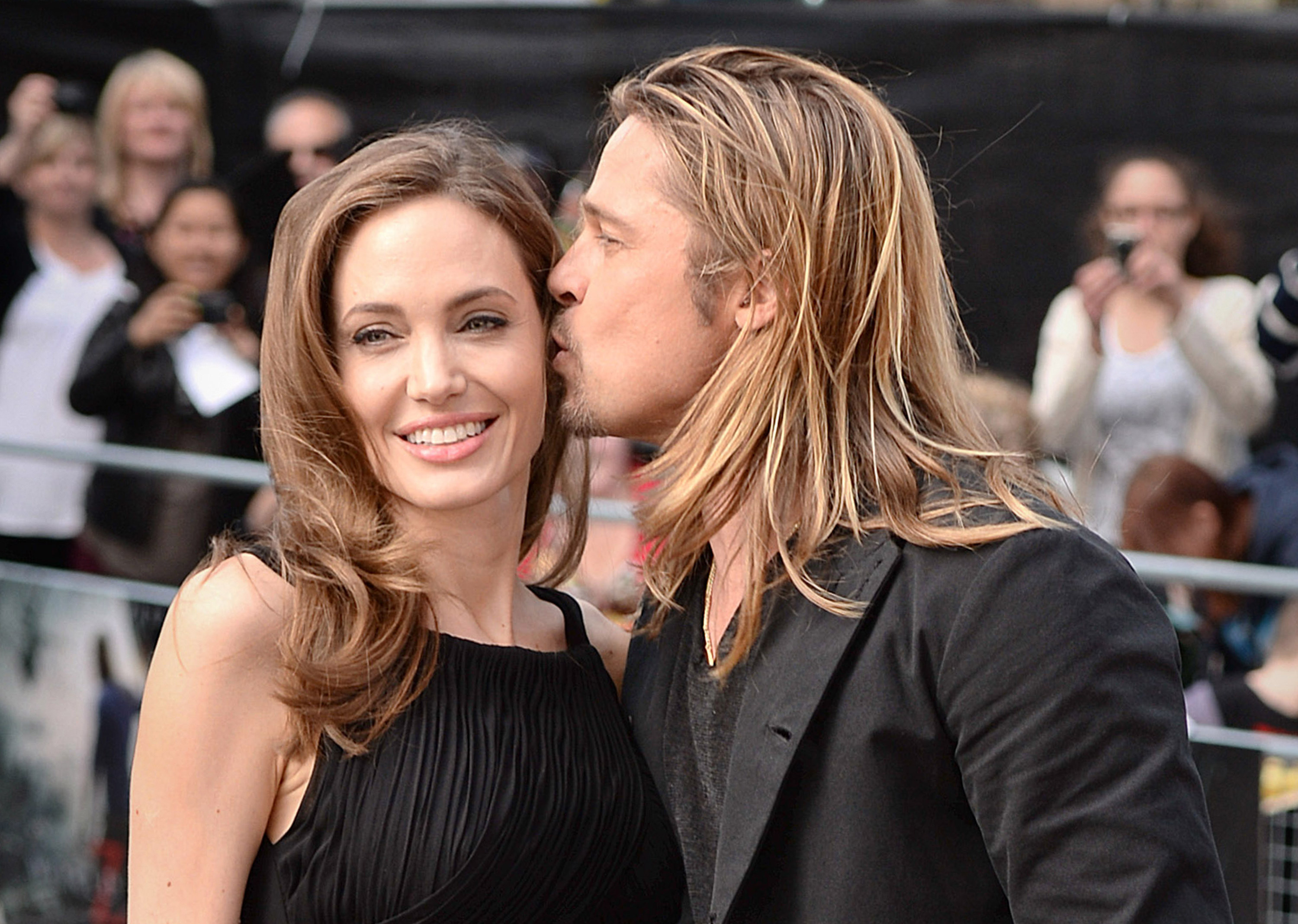 Angelina Jolie smiles while Brad Pitt leans in to give her a kiss on the cheek