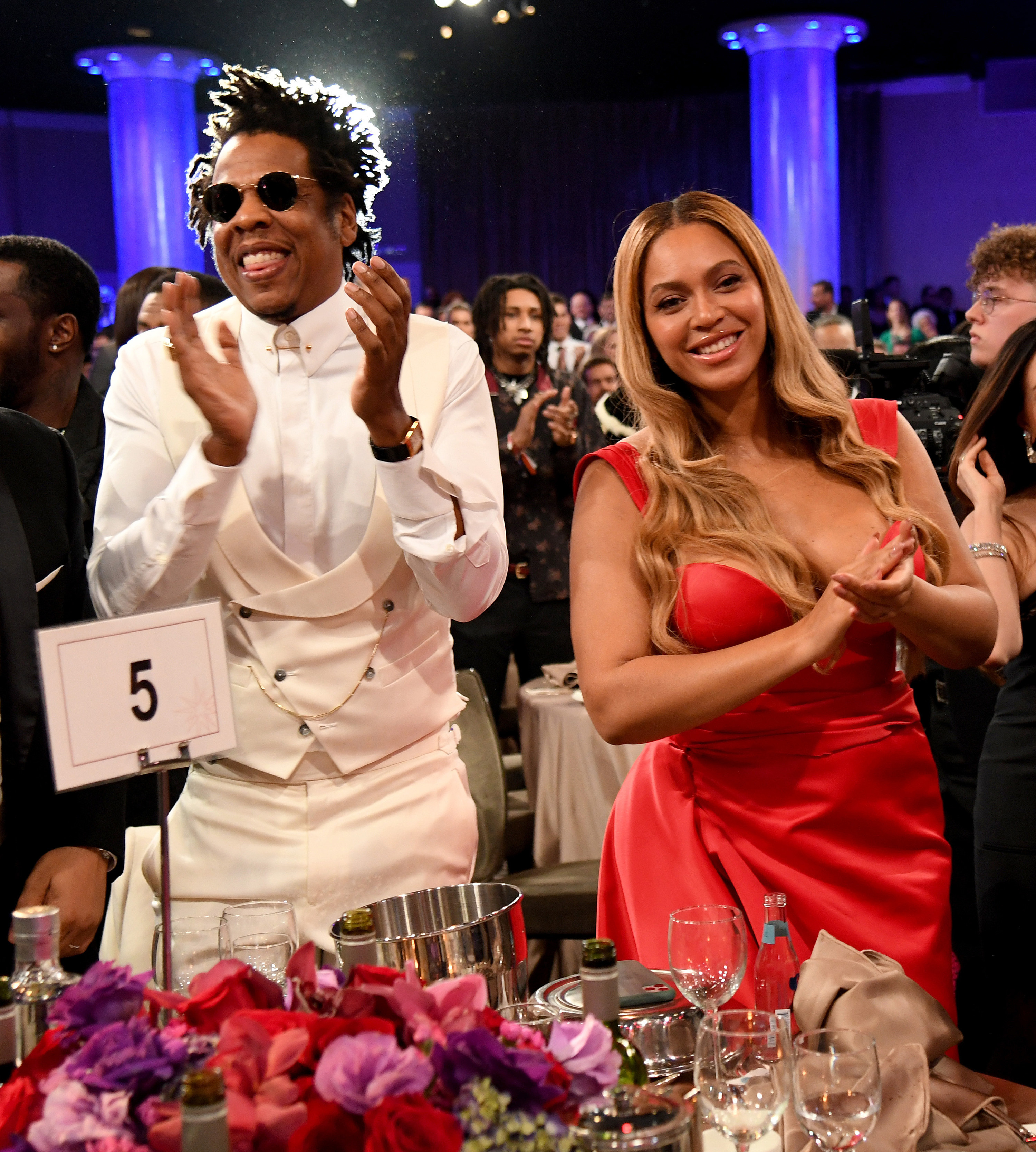 Jay-Z and Beyoncé stand and clap at a numbered table for an event
