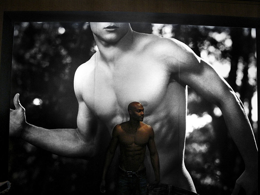 Model stands in front of the mural of a male torso at the entrance of an Abercrombie &amp;amp; Fitch