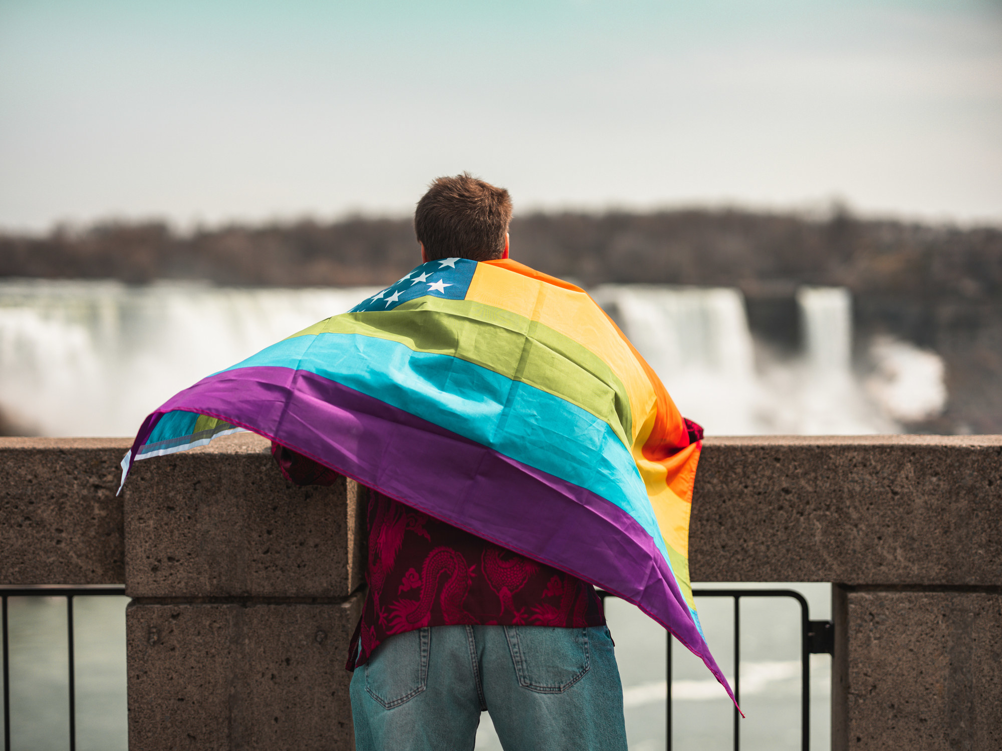 Gay man visiting Niagara Falls and holding a rainbow USA flag