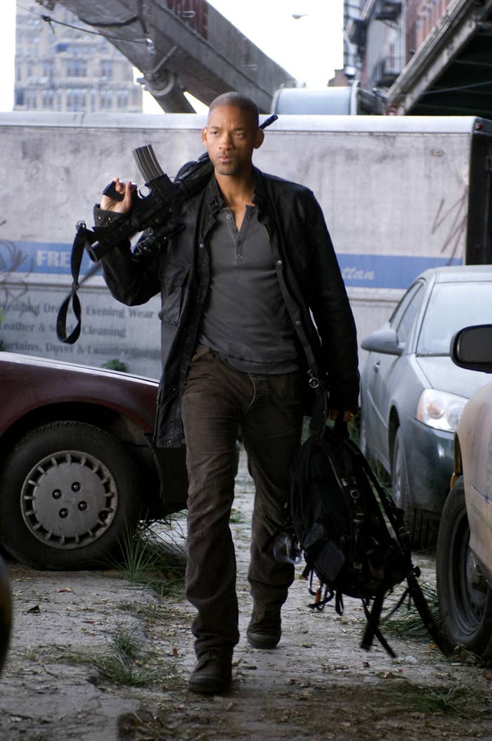 Will Smith carries a backpack in one hand and a gun over his shoulder in another