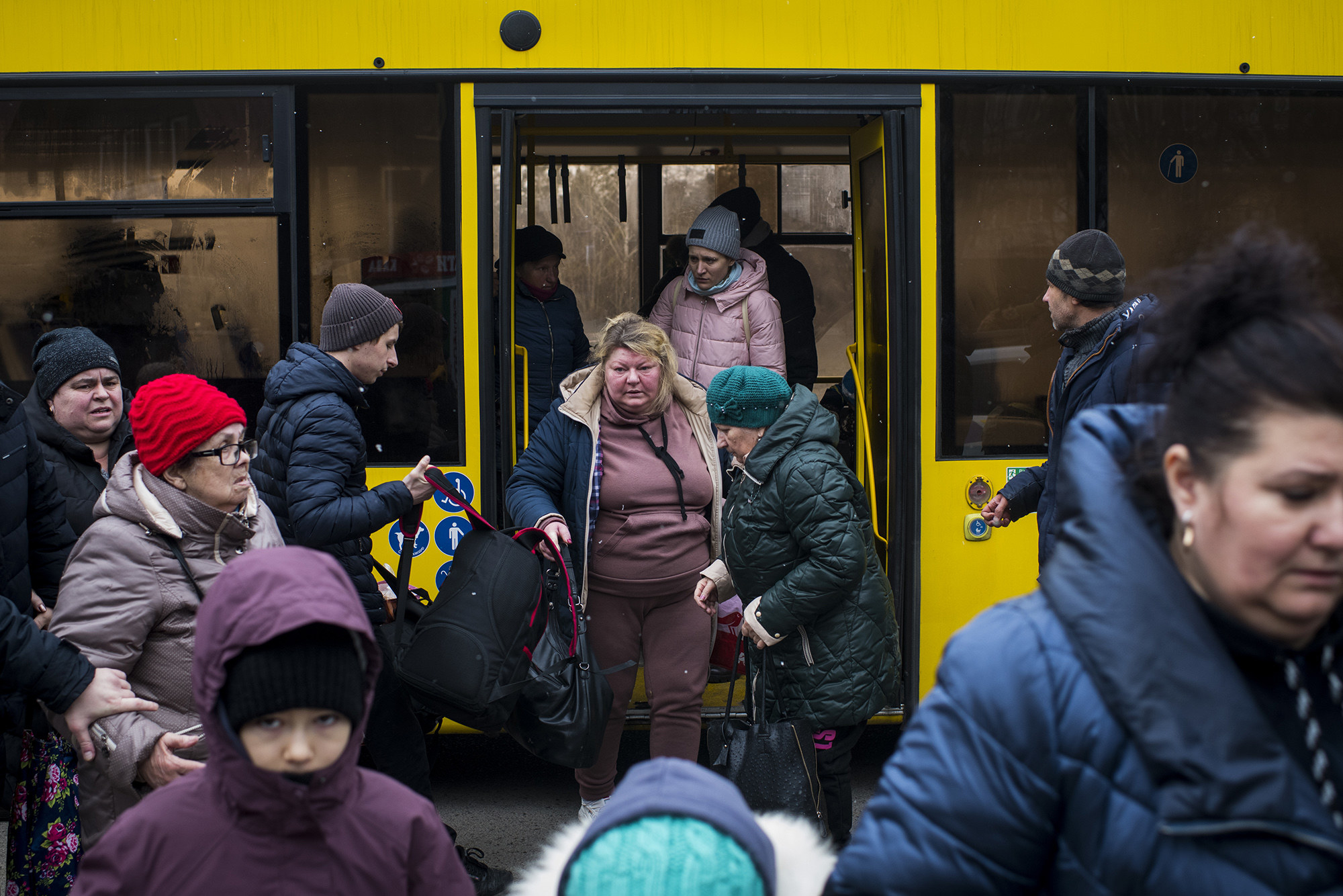 People, some elderly and carrying bags, emerge from a bus