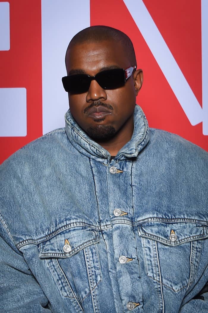 A closeup of Kanye wearing a denim jacket and dark sunglasses