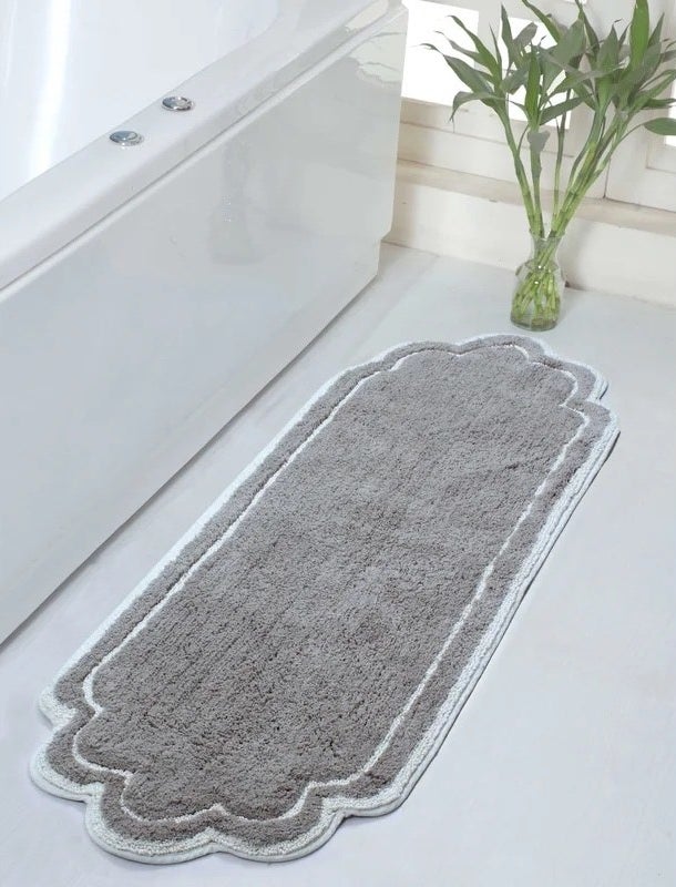 The dobrinka bath rug in gray next to a bathtub