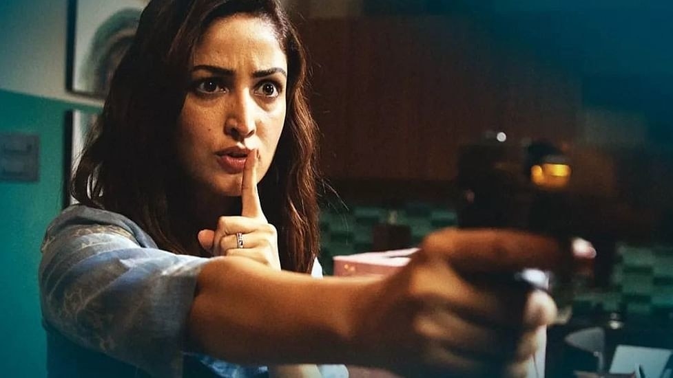 a woman pointing a gun with one hand and a finger to her lips in a &quot;shush&quot; motion with her other
