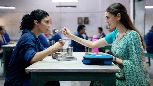 A woman in a sari spoon feeding a women in factory clothes