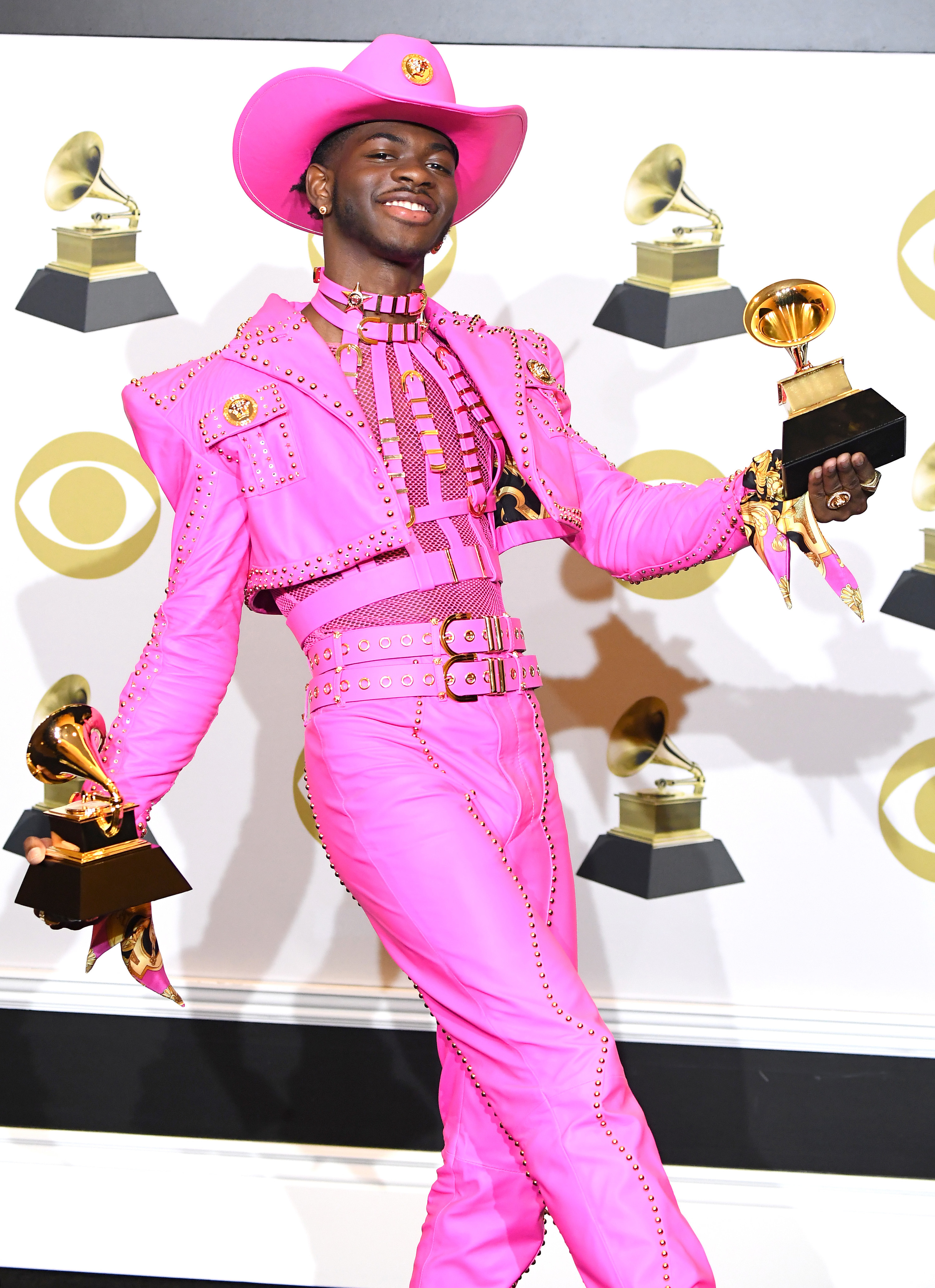 Lil Nas X holding his two Grammy awards backstage. He&#x27;s wearing a brightly-colored cowboy outfit complete with the hat