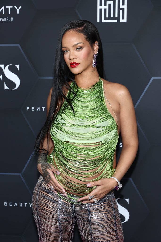 Rihanna cradling her baby bump as she poses on the red carpet in a fringed sequin top