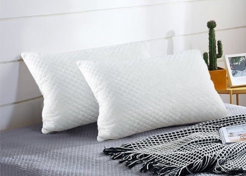 A pair of quilted pillows on a bed with a throw and magazine
