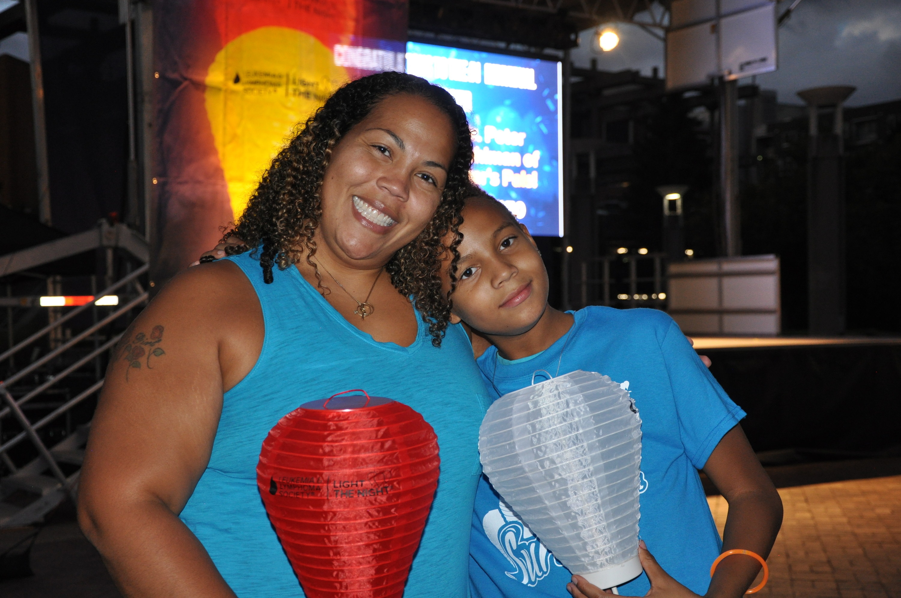 A mother and her son smiling at the camera while holding unlit paper lanterns
