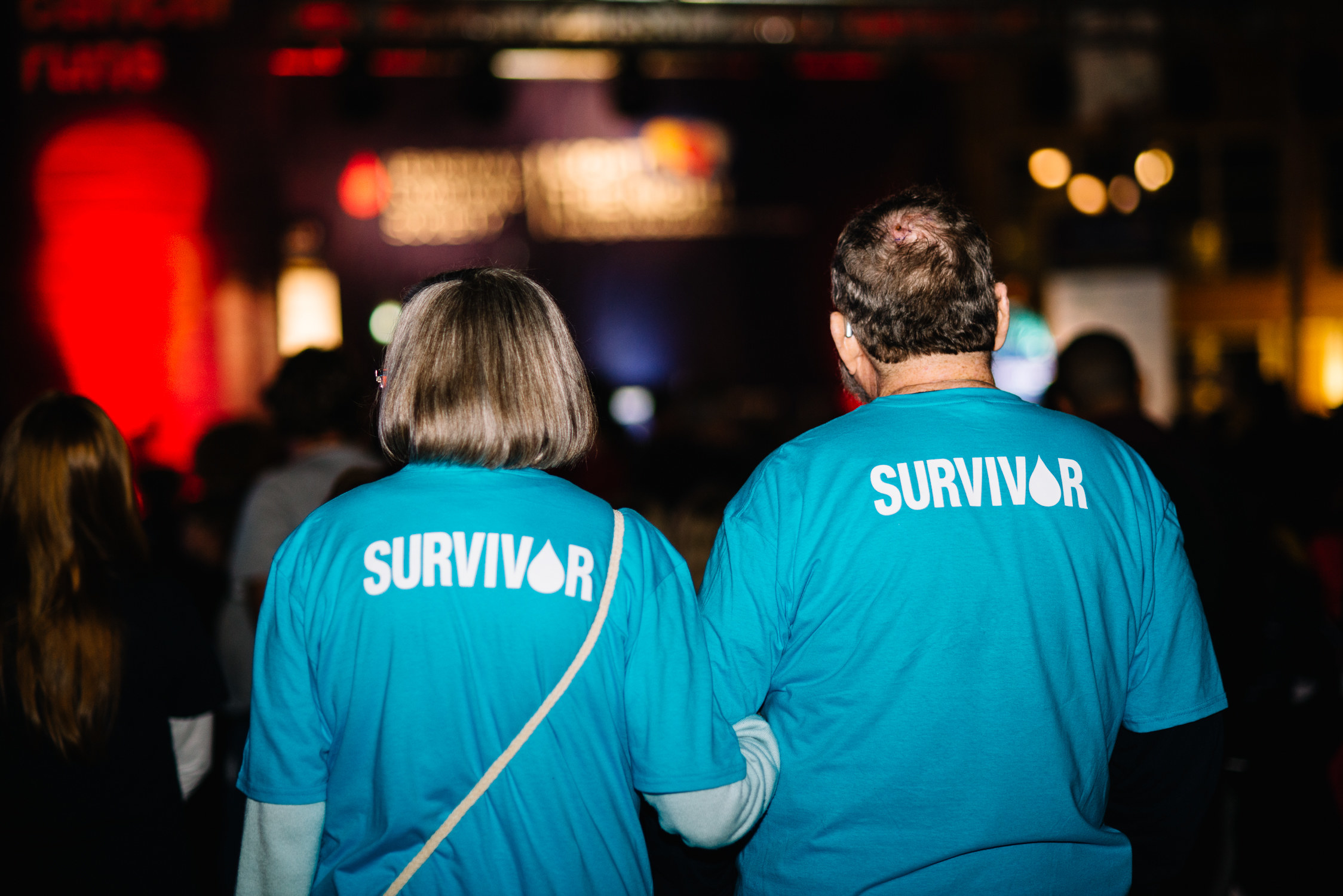 A man and a woman facing away from the camera showing the back of their shirts which read &quot;survivor&quot;