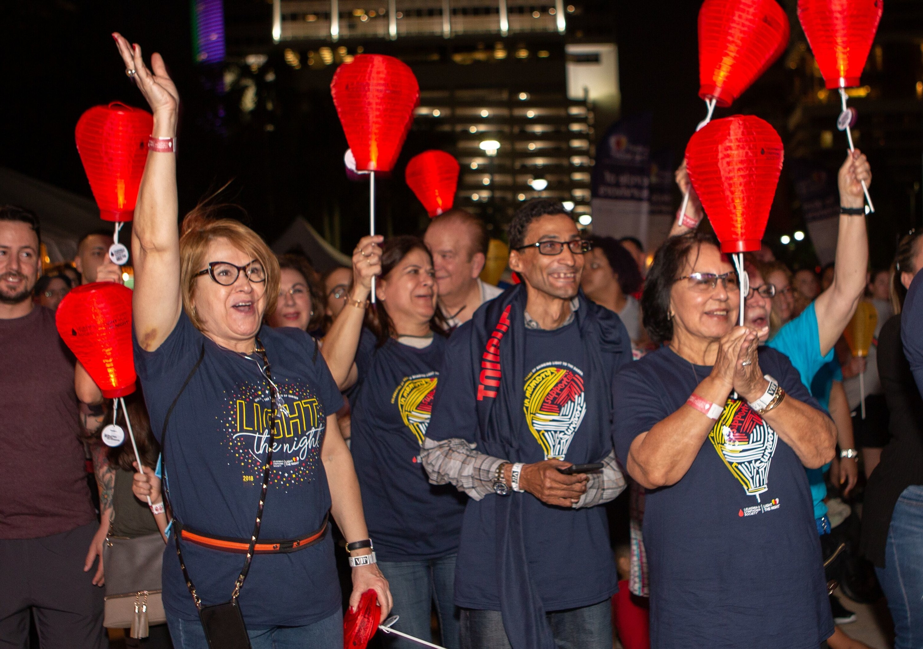 An excited crowd holding up lit paper lanterns at night