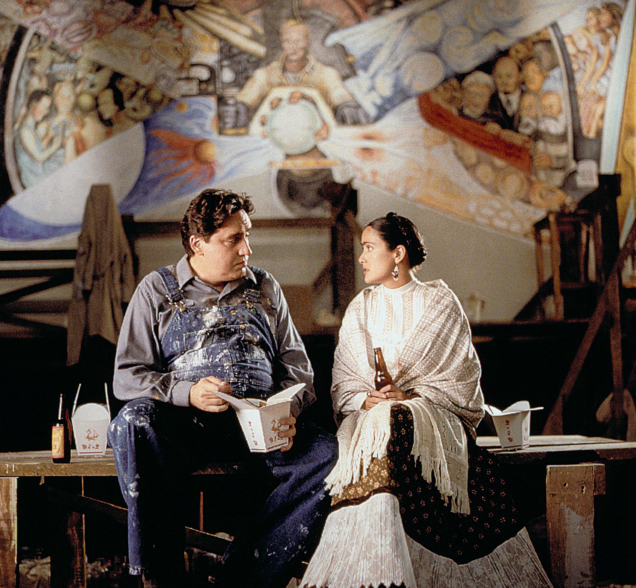 sitting together on a wooden bench, Diego and Frida share a dinner of Chinese takeout and a beer