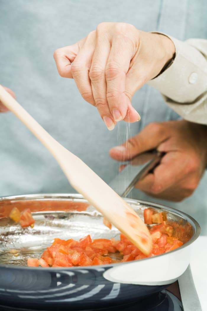 Sprinkling salt onto a pan of tomatoes.